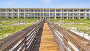 A wooden boardwalk leading to a multi-story hotel with balconies. - 🐬Crystal Sands 306B - Summer Salt | Gulf Views + Heated Community Pool (Destin)