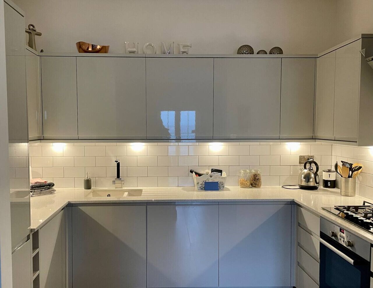 Une cuisine moderne avec des meubles gris, un plan de travail blanc et une cuisinière bien visible.