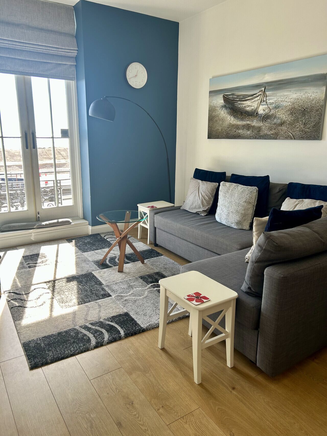 Un salon avec un canapé, une petite table, une lampe, une horloge et un tableau accroché au mur.