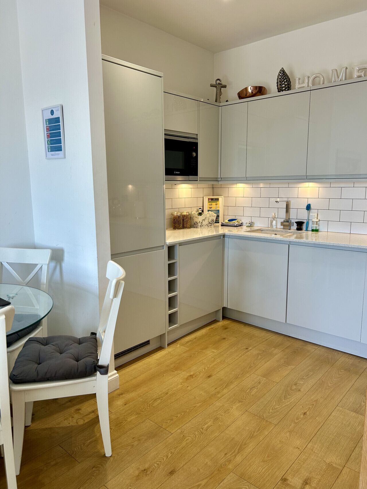 A modern kitchen with white cabinets, a Bosch microwave, and a dining area with a glass table and white chairs.