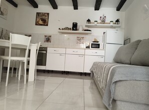 Eine moderne Küche mit weißen Schränken, einer Mikrowelle und einer Kaffeemaschine. Im Raum befinden sich ein weißer Stuhl und ein Sofa.