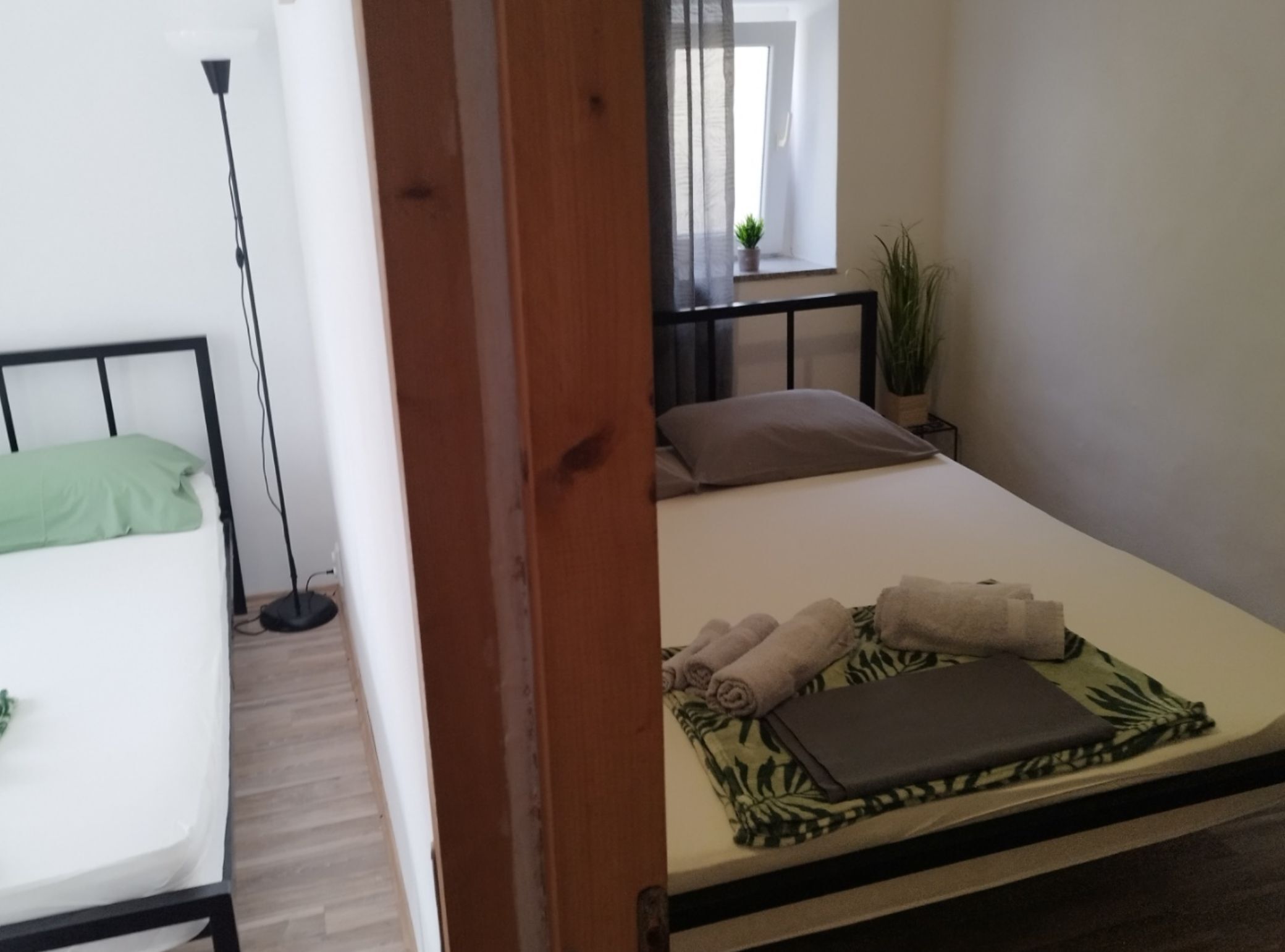 A bedroom with a bed, a bedside table, a potted plant, and a window with a view.