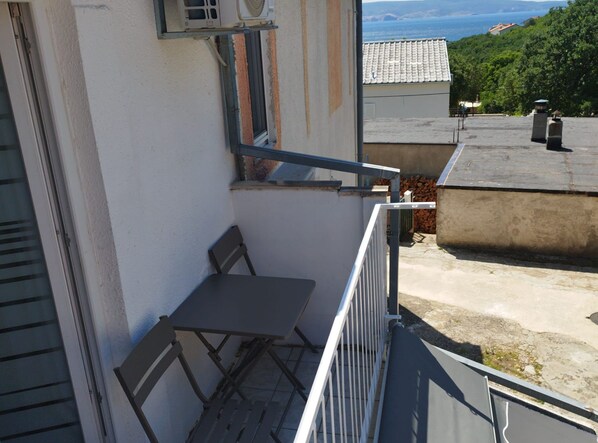 Ein Balkon mit Tisch und Stuhl, der auf einen Wohnbereich mit Häusern und Meerblick blickt.
