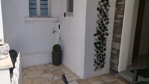 A small, enclosed outdoor area with a white wall, a window with shutters, a potted plant, and a sign reading "APARTMAN". - Apartment Leo Povile (Novi Vinodolski)