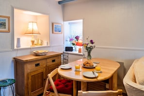 A dining area with a wooden table, chairs, a lamp, a vase with flowers, and a window with blinds.