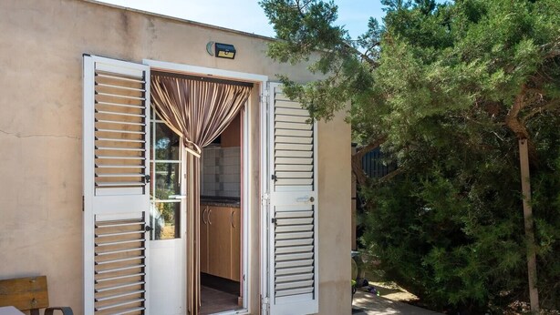 Un bâtiment doté d’une porte coulissante donnant sur un espace cuisine, d’une boîte aux lettres fixée au mur et d’un paillasson sur lequel est écrit « Bonjour ».