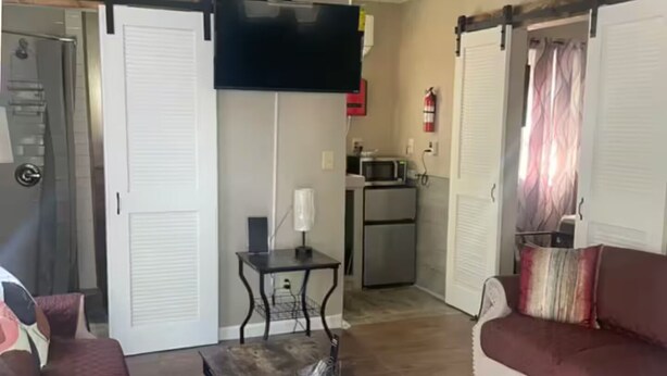 Una sala de estar con un sofá, una mesa de centro, un televisor montado en la pared y un ventilador de techo.