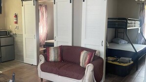 Un espacio habitable compacto con sofá, cama, ventilador de techo y kitchenette.