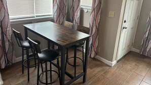 Un comedor con una mesa, cuatro sillas, una puerta y cortinas estampadas.