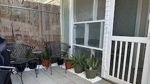 Un patio con mobiliario exterior, plantas en macetas y una cerca blanca.