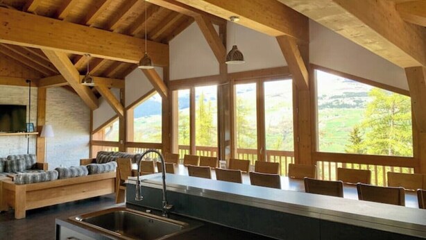 Una cocina con una isla grande, vigas de madera y ventanas amplias que dan a un paisaje verde.