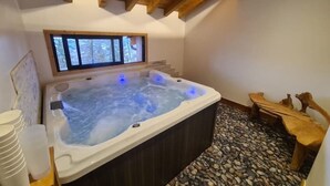 Un jacuzzi en una habitación con vigas de madera, una ventana y suelo de piedra.