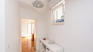 Ein Flur mit einem weißen Konsolentisch, einem Fenster mit Jalousien und einer Klimaanlage an der Wand.