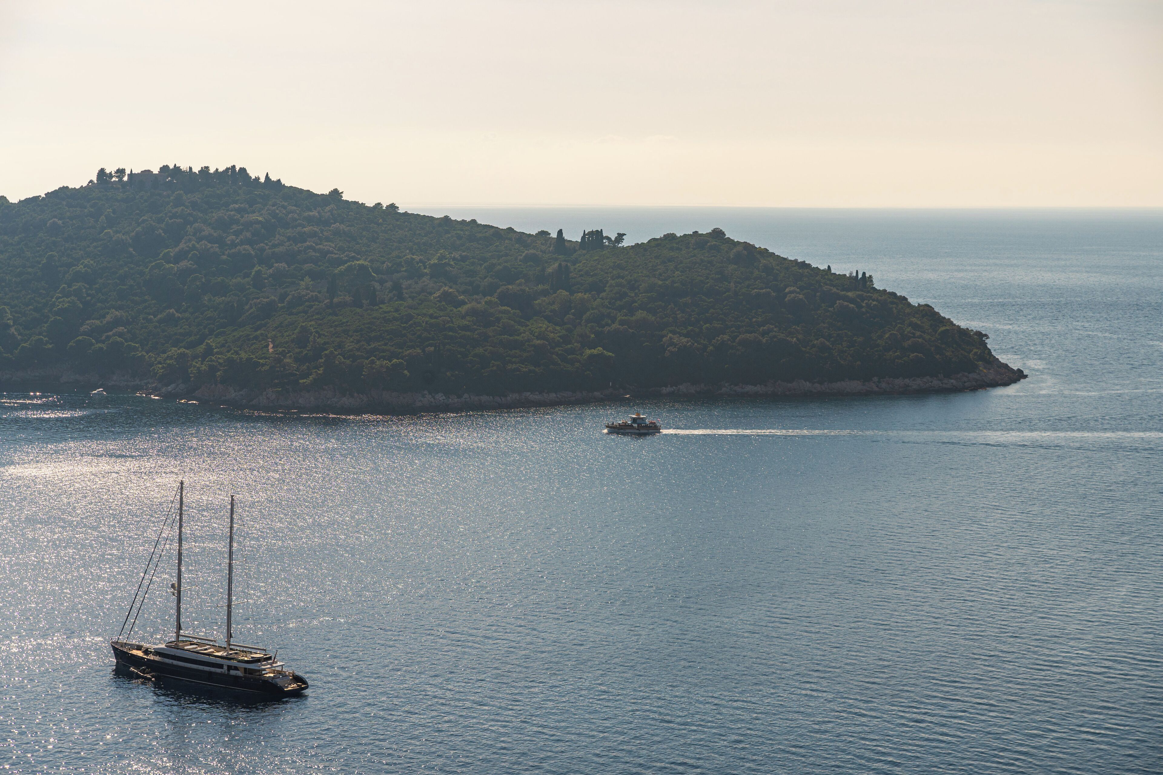 A sailboat on calm waters near a lush green island.