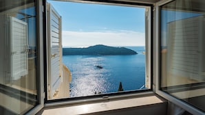 Ein Fenster mit Blick auf ein ruhiges Meer, eine kleine Insel und ein Segelboot.
