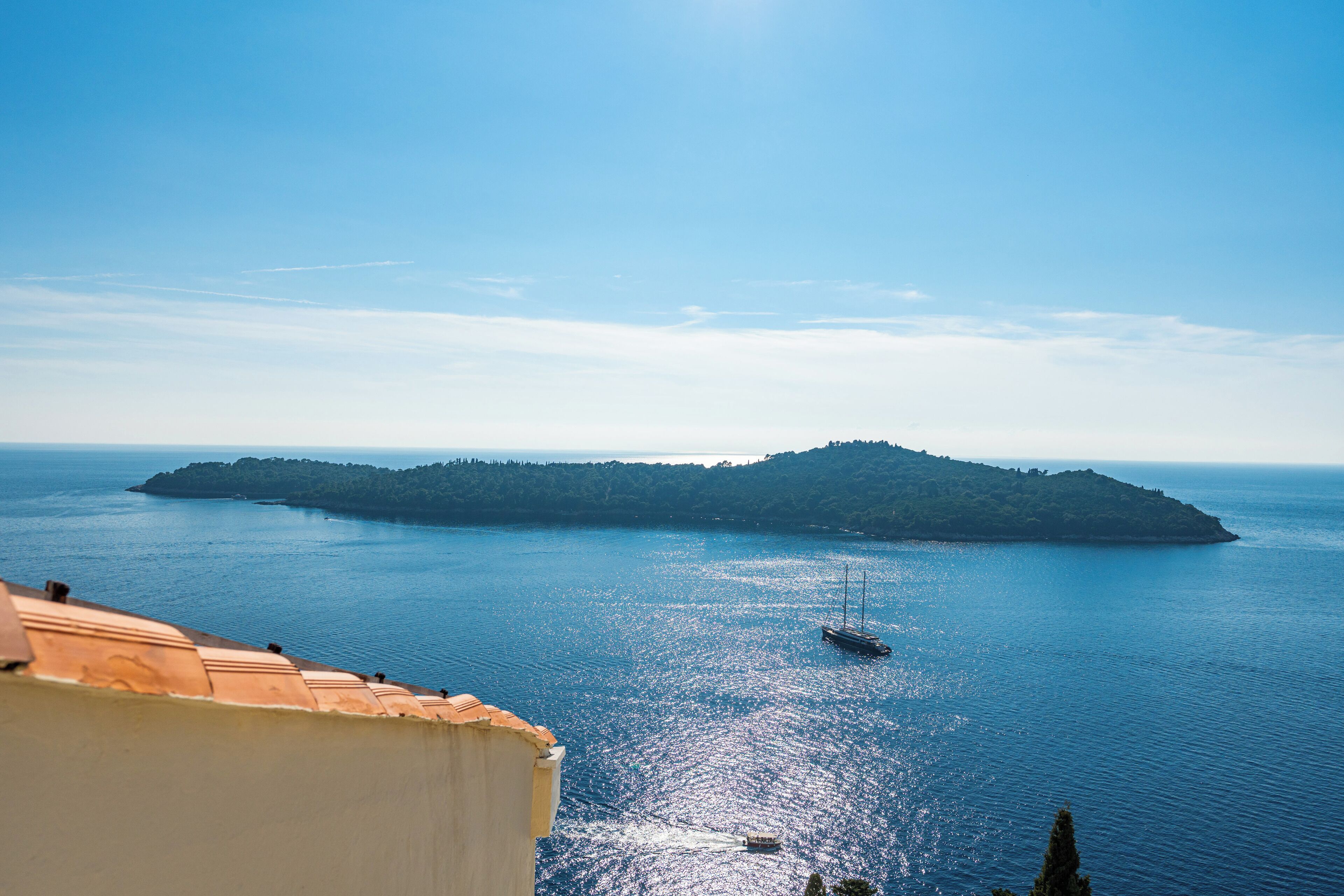 A coastal view with a large island, a boat, and a building with a sloped roof.