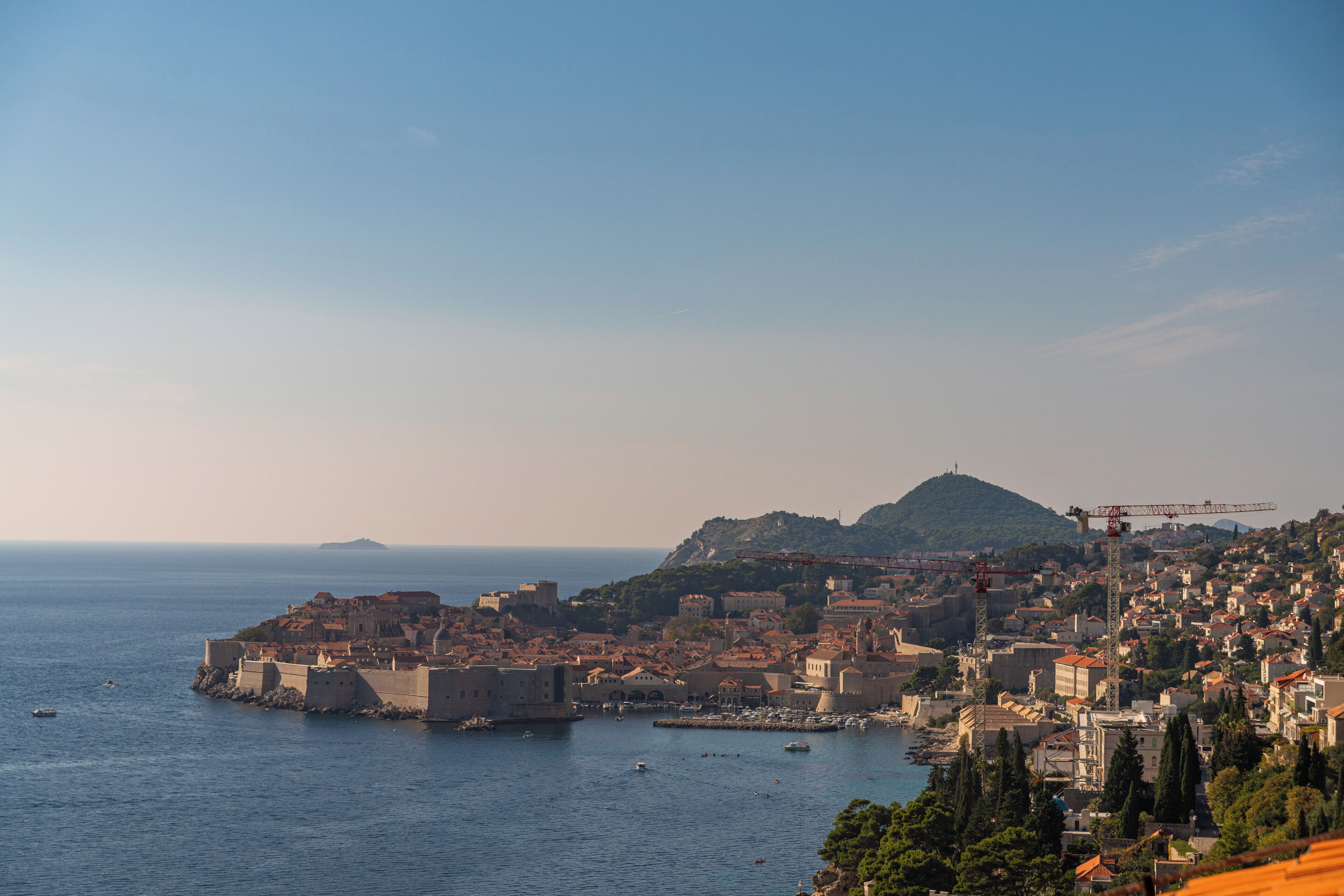 A coastal cityscape with historic buildings, a prominent hill, and a harbor with boats.