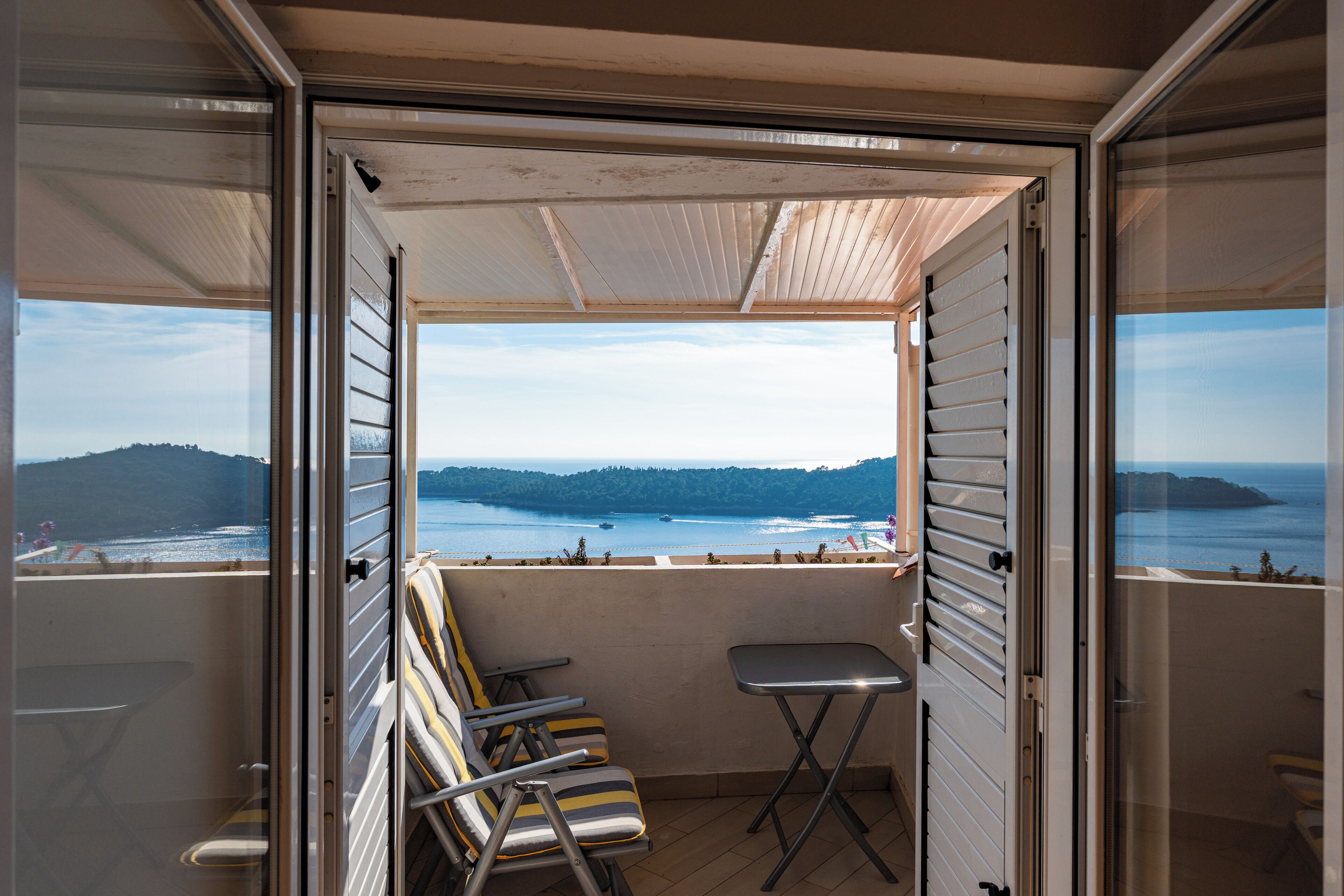 Un balcon avec vue sur la mer et les collines, deux chaises et une petite table.