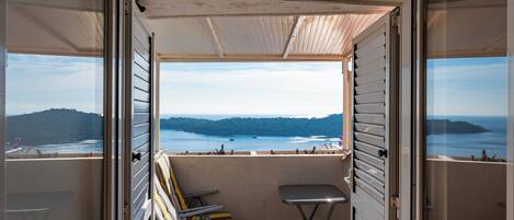 Un balcon avec vue sur la mer et les collines, deux chaises et une petite table.