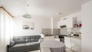 Eine moderne Küche mit weißen Schränken, einem grauen Sofa und einem Esstisch mit Stühlen.