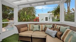 A covered outdoor seating area with a wicker sofa, cushions, and a view of a house and garden. - Pool and Hot Tub Walk to Ice Plant and Downtown (St. Augustine)