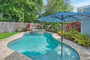 Ein Garten mit Swimmingpool, Whirlpool und Sonnenschirm.