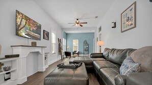 A modern living room with a sectional sofa, a fireplace, and a ceiling fan. - Pool and Hot Tub Walk to Ice Plant and Downtown (St. Augustine)