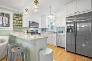 A modern kitchen with white cabinets, stainless steel appliances, and a marble countertop. - Mariners Cottage Steps to Sand Sparkling Pool (St. Augustine)