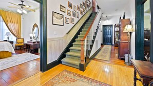A spacious room with a wooden floor, a staircase with a wooden handrail, and a large mirror.