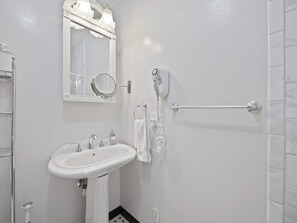 A bathroom with a white sink, a mirror with lights, a towel rack, and a hand dryer.