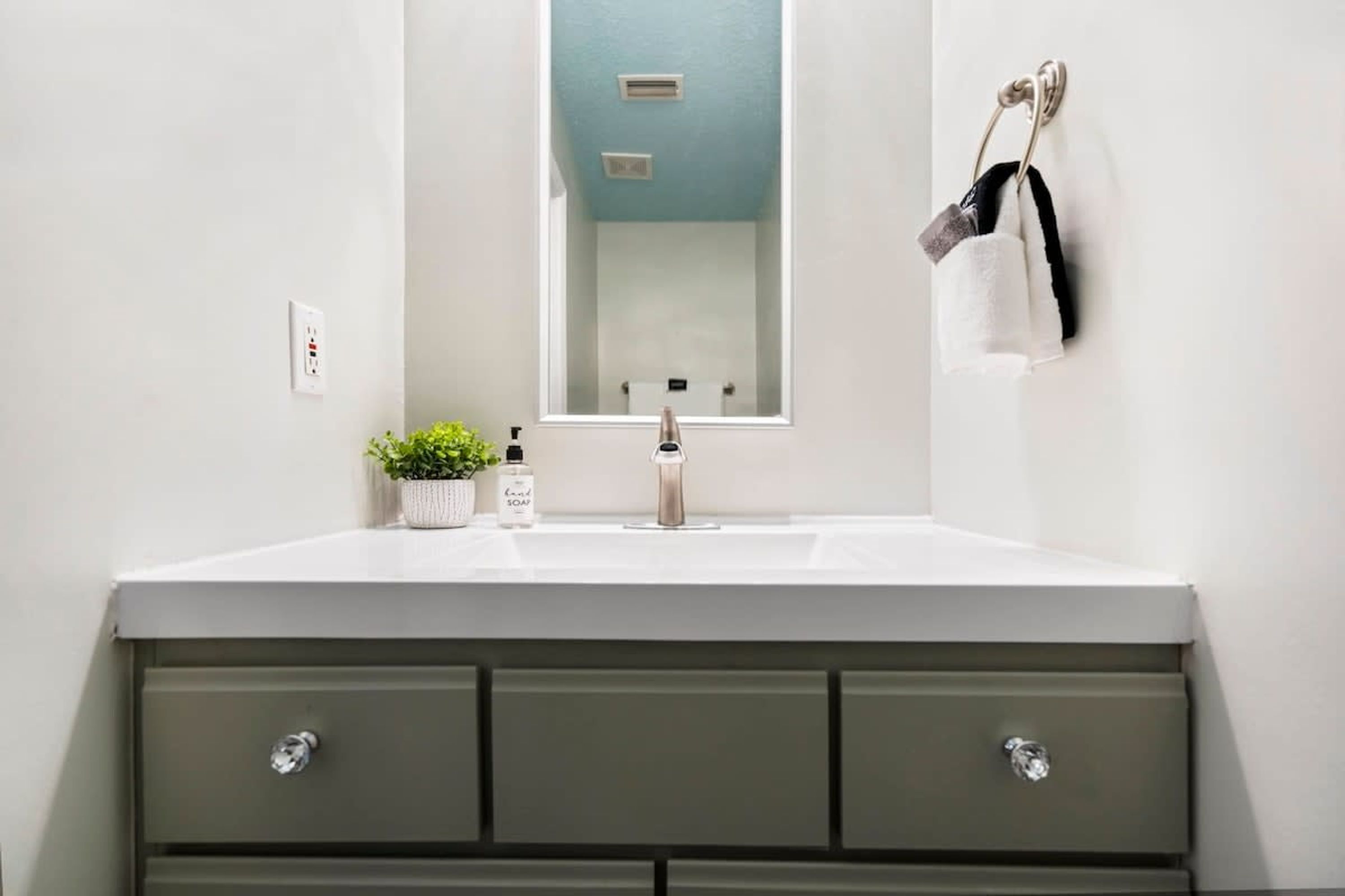 A bathroom with a white sink, a mirror, and a green vanity with drawers.