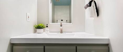 A bathroom with a white sink, a mirror, and a green vanity with drawers.