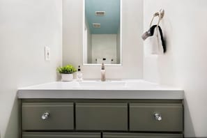 Une salle de bain avec un lavabo blanc, un miroir et une commode verte dotée de tiroirs.
