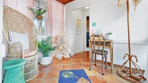 Une pièce chaleureuse avec des fauteuils en osier, un petit sapin de Noël blanc et un sol orné d’un motif de carreaux bleus et oranges.