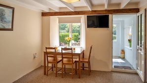Un coin repas avec une table et des chaises en bois, une fenêtre donnant sur un paysage verdoyant et un téléviseur fixé au mur.