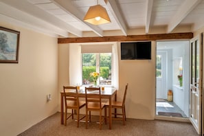 Ein Essbereich mit Holztisch und -stühlen, einem Fenster mit Blick ins Grüne und einem an der Wand befestigten Fernseher.