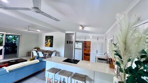 Una cocina moderna con una isla central, armarios blancos y una zona de comedor con un sofá azul.