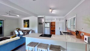 Una cocina moderna con una isla central, armarios blancos y un comedor con un sofá azul.