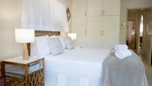 Un lit bien fait, avec du linge de lit blanc, une table de chevet avec une lampe et une armoire avec un miroir.
