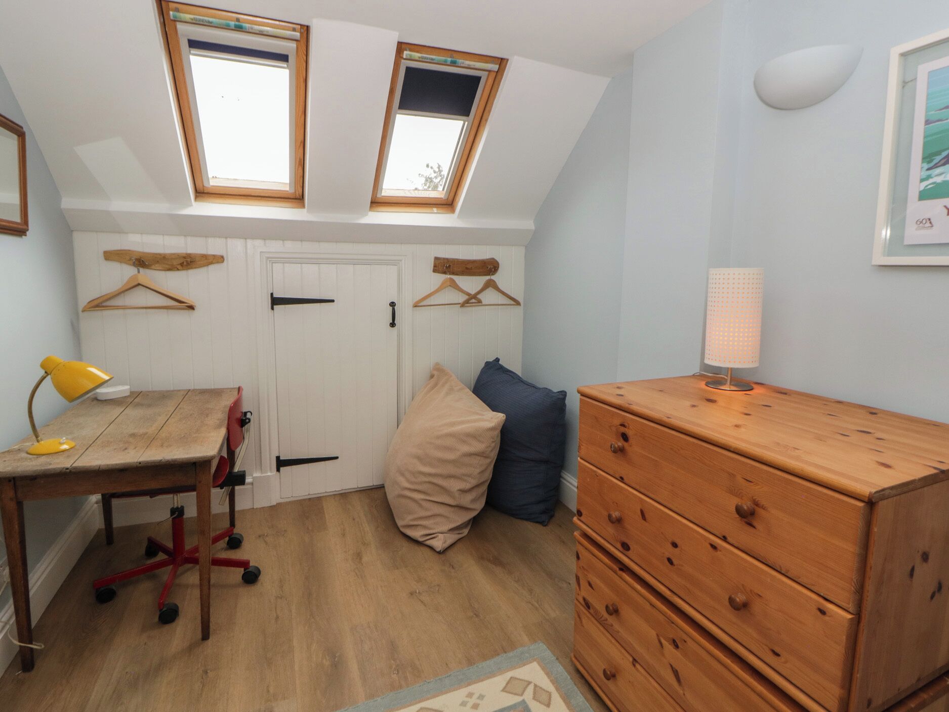 A room with a desk, chair, dresser, two hanging clothes racks, and a skylight.
