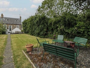 A garden with a pathway leading to a building, green benches, and a potted plant. - Ty Clyd (Newport)