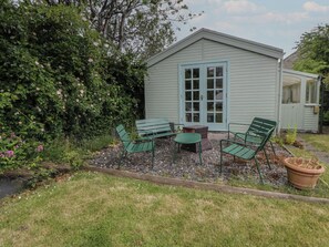 A small shed with a door and windows, surrounded by a garden with a bench and a table. - Ty Clyd (Newport)