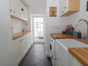 A kitchen with white cabinets, a washing machine, a wooden countertop, and a poster advertising Southwold bottled beers.