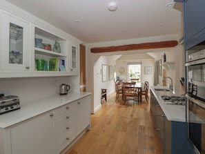 Une cuisine avec des meubles blancs, une table à manger en bois et une cuisinière encastrée.