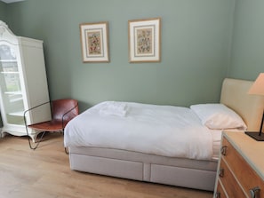 A bedroom with a bed, a chair, a dresser, and two framed floral pictures on the wall. - Ty Clyd (Newport)