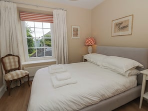 Une chambre à coucher avec un grand lit, une chaise, une fenêtre avec des rideaux, une lampe de chevet et un tableau encadré au mur.