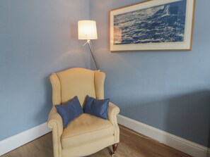 A beige armchair with blue cushions, a floor lamp, and a framed picture of the ocean on a blue wall. - Ty Clyd (Newport)