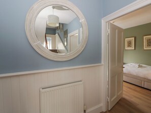 A room with a white radiator, a round mirror on the wall, and a bed with white bedding. - Ty Clyd (Newport)