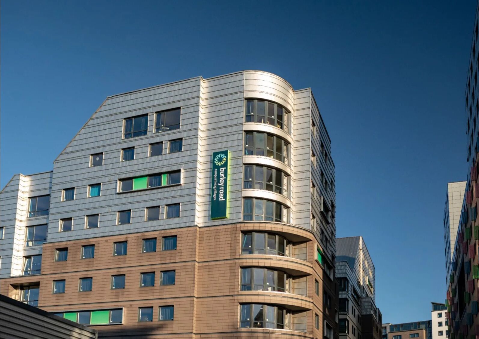 Un edificio moderno con una facciata curva, diverse finestre e un cartello con la scritta 'Burley Road Campus Hotels'.
