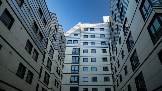En moderne bygning med flere etager, symmetrisk facade, store vinduer og en klar himmel.